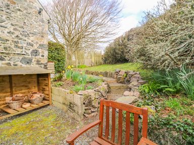 A garden with a wooden chair stone steps and a wood storage shed at Higher Lampra in Mullion
