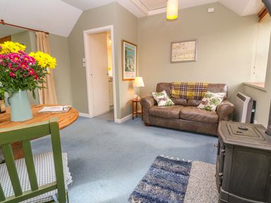 A living room with a brown leather sofa and a wood stove at Higher Lampra in Mullion