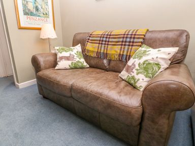A brown leather sofa with two patterned cushions and a plaid throw next to a lamp and framed picture at Higher Lampra in Mullion