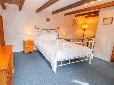 A bedroom with a metal bed frame white bedding wooden nightstands lamps and wooden beams on the ceiling at Higher Lampra in Mullion
