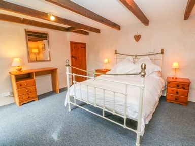 A bedroom with a white metal bed frame bedside tables with lamps a wooden desk and a wall mirror at Higher Lampra in Mullion