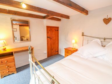 A bedroom with a bed a desk a chair a mirror and wooden beams on the ceiling at Higher Lampra in Mullion