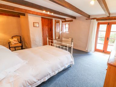 A bedroom with a double bed wooden beams on the ceiling a chair a door and French doors at Higher Lampra Mullion