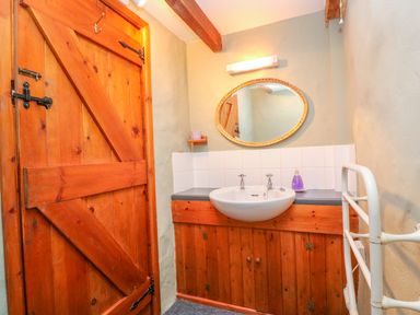 A bathroom with a wooden door a sink with a mirror above and a white towel rack at Higher Lampra in Mullion