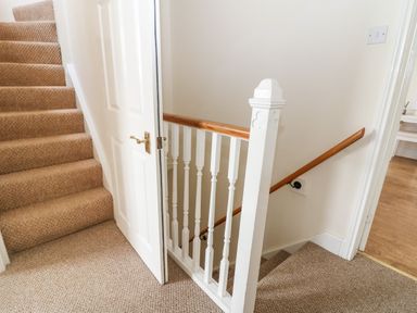A carpeted staircase with a white door and wooden handrail next to a hallway with wooden flooring at The Cottage at Broadway in Broadway