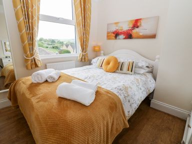 A bedroom with a bed with yellow and white bedding yellow curtains a window and a painting above the bed at The Cottage at Broadway in Broadway