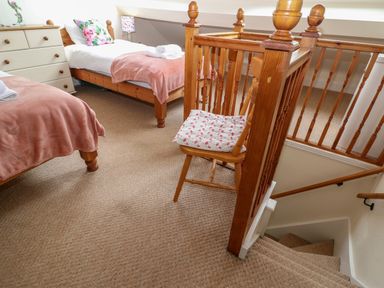 A bedroom with two single beds a chest of drawers a chair on a carpeted floor and a staircase at The Cottage at Broadway
