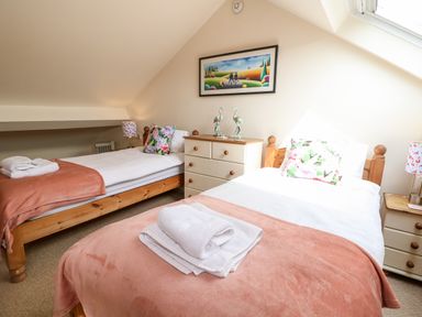 A bedroom with two single beds with pink blankets and floral pillows a chest of drawers with flamingo ornaments and a framed painting on the wall at The Cottage at Broadway in Broadway