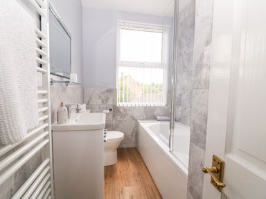 A bathroom with a bathtub shower combination a toilet a sink a mirror and a window with vertical blinds at The Cottage at Broadway in Broadway