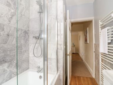 A bathroom with a bathtub and shower head next to a hallway with a small chest of drawers at The Cottage at Broadway in Broadway