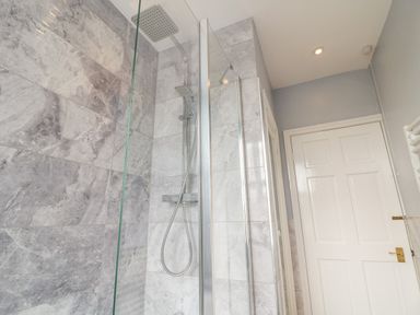 A bathroom shower area with a glass partition a rainfall showerhead marble tiled walls and a white door at The Cottage at Broadway in Broadway