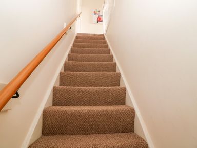 A carpeted staircase with wooden handrail and white walls at The Cottage at Broadway in Broadway