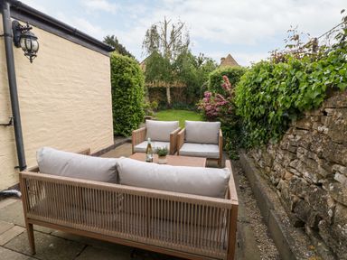 An outdoor patio with cushioned seating and a wooden table next to a stone wall and garden at The Cottage at Broadway in Broadway