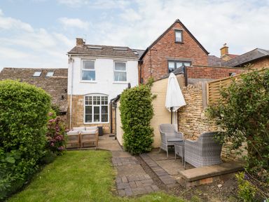 A backyard garden with patio furniture and umbrellas next to a brick and white house at The Cottage at Broadway