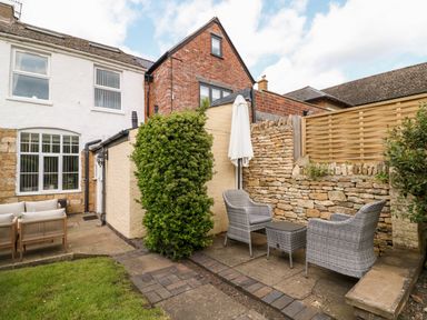 An outdoor patio area with two wicker chairs a small table an umbrella a stone wall and part of a house at The Cottage at Broadway in Broadway