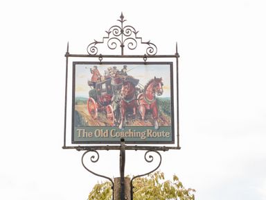 A street sign with an illustration of a horse-drawn carriage labeled The Old Coaching Route