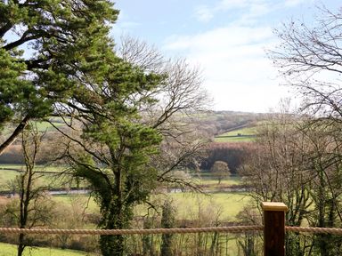 A view of a green hilly landscape with trees and a rope fence in the foreground at Little Silver Leaf in High Bickington