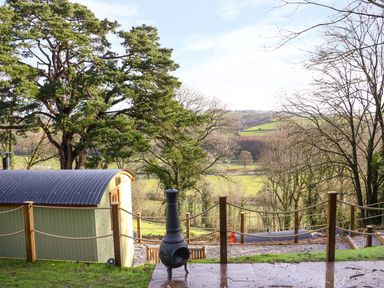 An outdoor patio with a chiminea and a fenced area overlooking fields and trees at Little Silver Leaf in High Bickington