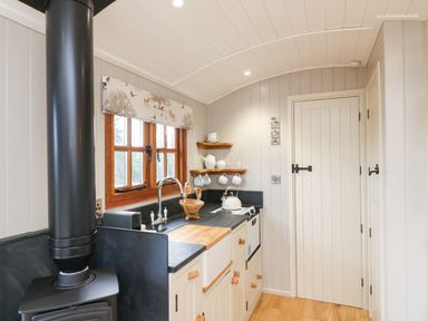 A kitchen with a wood stove sink shelves with cups and teapots and a window at Little Silver Leaf in High Bickington