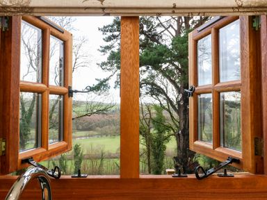 A wooden framed window open to a view of trees and fields at Little Silver Leaf in High Bickington