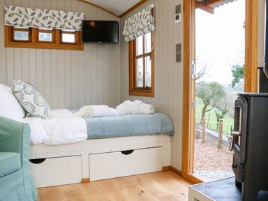 A small bedroom with a single bed a green chair a wall-mounted tv and a door leading outside at Little Silver Leaf in High Bickington
