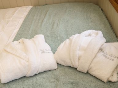 Two white bathrobes laid out on a bed with a green cover at Little Silver Leaf in High Bickington
