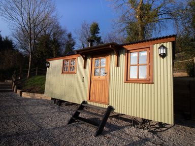 A small green corrugated metal cabin with wooden framed windows and door on gravel at Little Silver Leaf in High Bickington