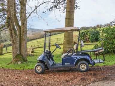 A golf cart parked on a dirt path near trees and green fields at Little Silver Owl in High Bickington