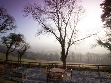 An outdoor seating area with wooden table and chairs surrounded by trees and a wooden fence at Little Silver Owl in High Bickington