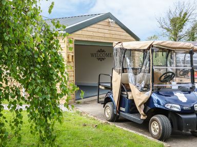 A golf cart parked on a driveway outside a wooden garage with welcome sign at Little Silver Owl in High Bickington