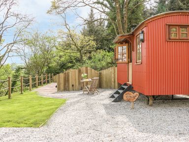 An outdoor area with a red metal cabin a wooden table and chairs and a wooden fence at Little Silver Owl in High Bickington