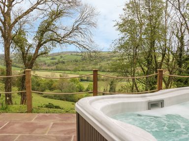 An outdoor hot tub on a tiled patio overlooking green fields and trees at Little Silver Owl in High Bickington