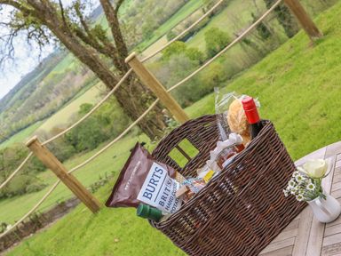 A picnic basket with snacks and beverages on a wooden table outdoors at Little Silver Owl in High Bickington
