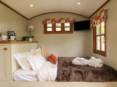 A bedroom with a bed pillows robes on the bed and a TV on the wall at Little Silver Owl in High Bickington