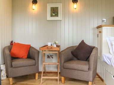 A pair of armchairs with cushions and a small wooden table in between in a room at Little Silver Owl in High Bickington