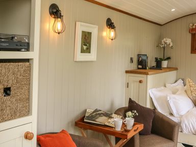 A corner of a room with two armchairs a small wooden table with cups and books wall lights and a bed with pillows at Little Silver Owl in High Bickington