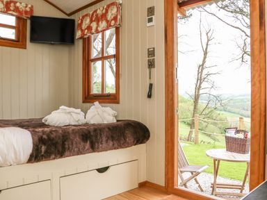 A bedroom with a bed robes on it TV on the wall and an open door leading to a table and chairs outside at Little Silver Owl in High Bickington