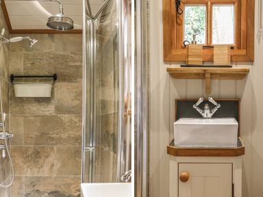 A bathroom shower area with tiled walls and a small sink with wooden framed window at Little Silver Owl in High Bickington