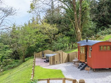 A red shepherds hut with steps and outdoor seating near a fenced grassy area at Little Silver Owl in High Bickington