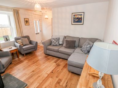 A living room with gray sofas wooden floor wooden side table and a lamp at Coeden Bach in Burry Port