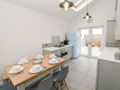 A kitchen with a wooden dining table set for six people a light blue fridge a gas stove and double glass doors leading outside at Coeden Bach in Burry Port