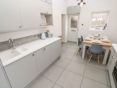 A kitchen with grey cabinets and a dining table set with plates and glasses at Coeden Bach in Burry Port