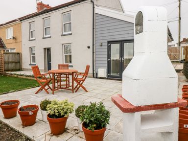An outdoor patio with wooden table and chairs surrounded by potted plants and a white outdoor heater at Coeden Bach in Burry Port