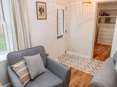 A sitting area with gray armchair and two cushions next to a door with patterned floor tiles and wooden flooring at Coeden Bach in Burry Port