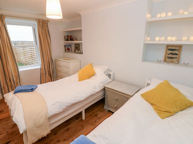 A bedroom with two single beds yellow pillows and a window with striped curtains at Coeden Bach in Burry Port