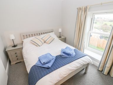 A bedroom with a double bed two bedside tables with lamps and a window with curtains at Coeden Bach in Burry Port