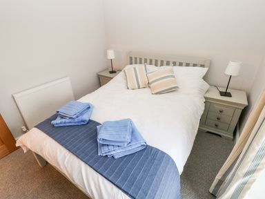 A bedroom with a double bed two bedside tables with lamps folded towels on the bed at Coeden Bach in Burry Port