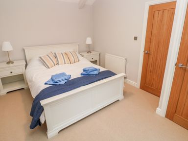 A bedroom with a white bed with striped pillows and blue towels on the bed with two white bedside tables with lamps at Coeden Bach in Burry Port