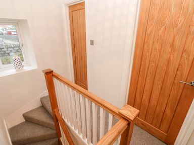 A stairway with carpeted steps and wooden banister next to wooden doors and a window with a vase on the sill at Coeden Bach in Burry Port