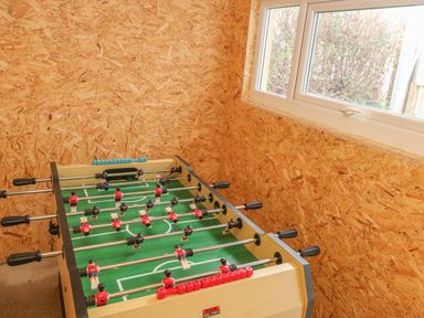 A foosball table in a room with wood panel walls and a window at Coeden Bach in Burry Port
